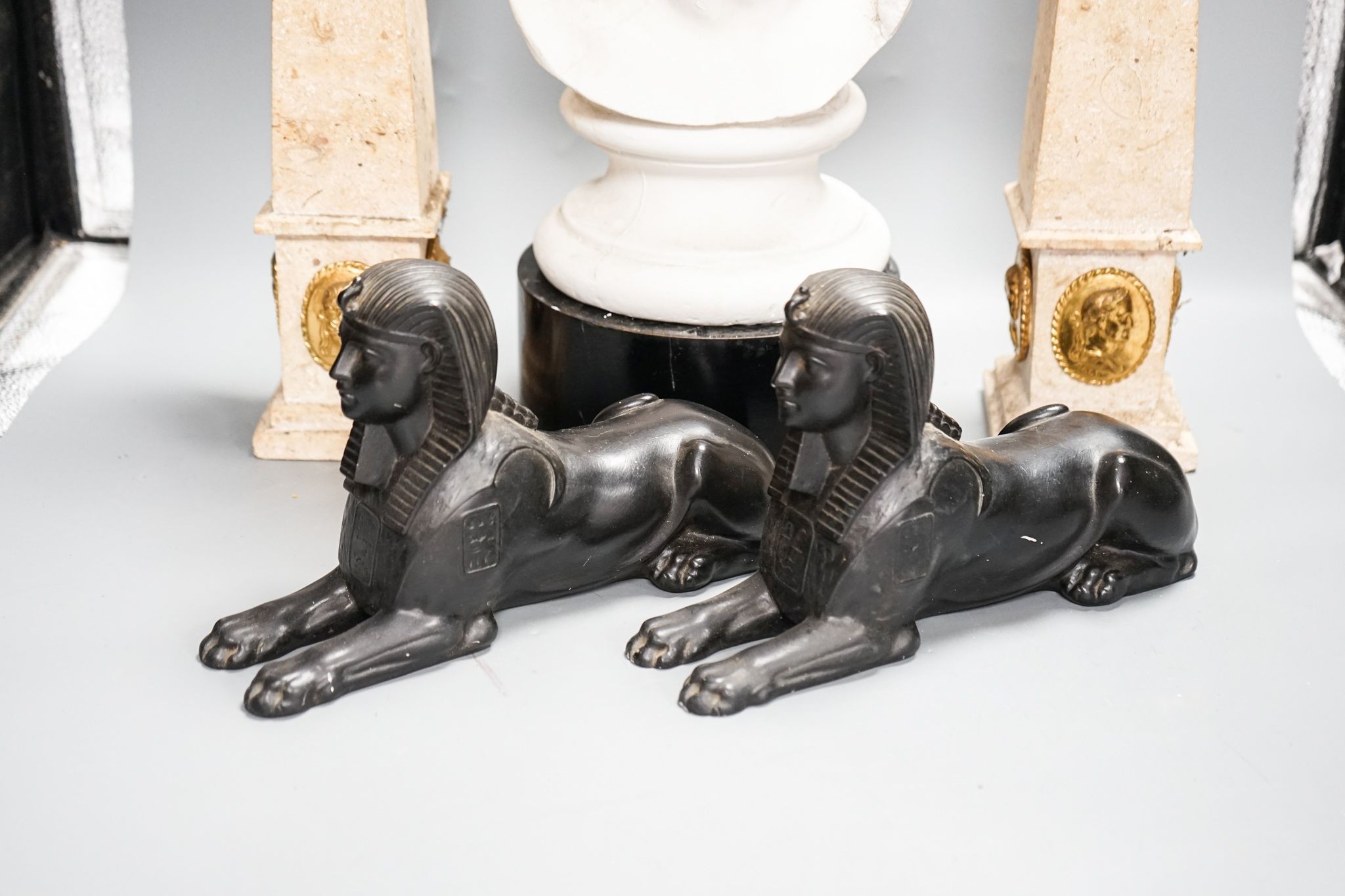 A pair of composition classical faux marble obelisks together with a pair of simulated stone Sphinx, a faux bronze model of Trajan‘s column and a faux marble bust (5)